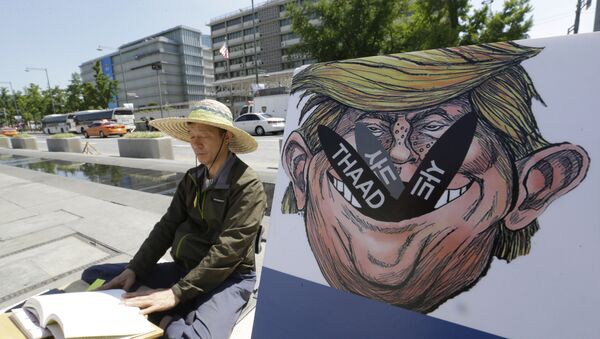 A South Korean protester sits next to a poster with an illustration of U.S. President Donald Trump to oppose a plan to deploy an advanced U.S. missile defense system called Terminal High-Altitude Area Defense, or THAAD, near the U.S. Embassy in Seoul Monday, June 5, 2017 - Sputnik International