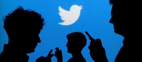 People holding mobile phones are silhouetted against a backdrop projected with the Twitter logo. (File) - Sputnik International