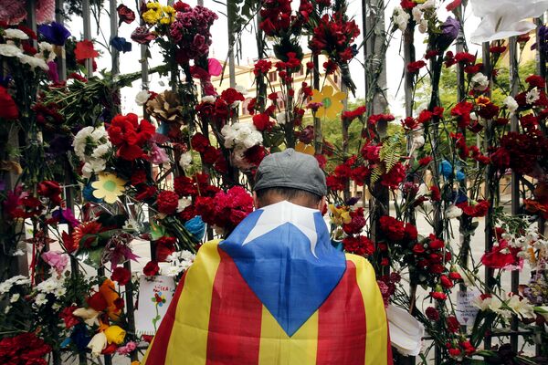 A man wrapped in a Catalan pro-independence 'Estelada' flag puts flowers on the gate of Barcelona's Ramon Llull School, which was used as a polling station and was one of those targeted by riot police during the October 1 banned independence referendum, as Catalonia observes a general strike called by Catalan unions on October 3, 2017 - Sputnik International