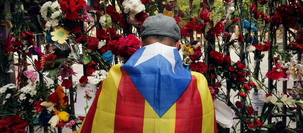 A man wrapped in a Catalan pro-independence 'Estelada' flag puts flowers on the gate of Barcelona's Ramon Llull School, which was used as a polling station and was one of those targeted by riot police during the October 1 banned independence referendum, as Catalonia observes a general strike called by Catalan unions on October 3, 2017 - Sputnik International