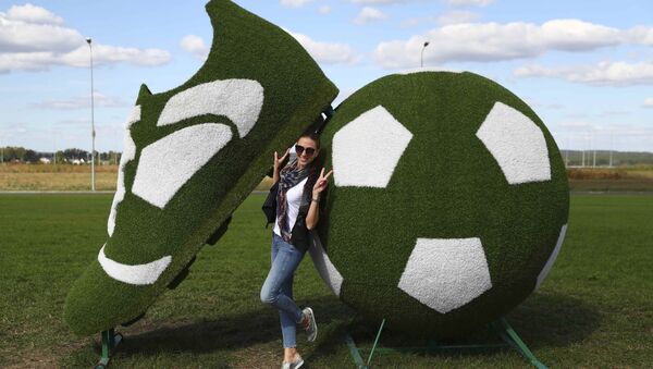 A woman poses for a picture near a decorative sculpture, depicting a ball and a soccer boot, near a terminal of Kurumoch International Airport outside Samara, the host city for the 2018 FIFA World Cup, Russia, September 17, 2017 - Sputnik International