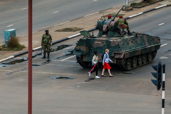 Young women walk past an armoured personnel carrier that stations by an intersection as Zimbabwean soldiers regulate traffic in Harare on November 15, 2017 Young women walk past an armoured personnel carrier that stations by an intersection as Zimbabwean soldiers regulate traffic in Harare on November 15, 2017 - Sputnik International