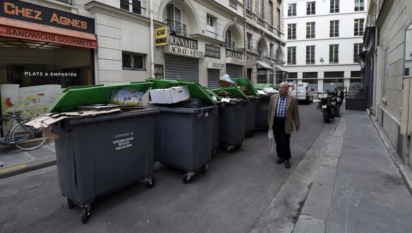 (File) A pedestrians walks past unemptied garbage bins and plastic bags during a strike of garbage collectors in a street in Paris on October 8, 2015 - Sputnik International