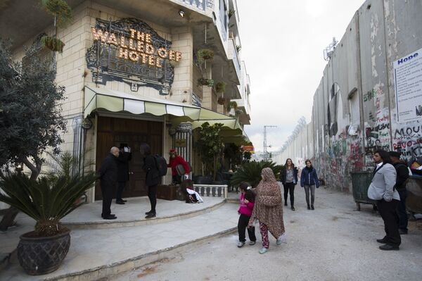 People pass by the The Walled Off Hotel and the Israeli security barrier in the West Bank city of Bethlehem - Sputnik International