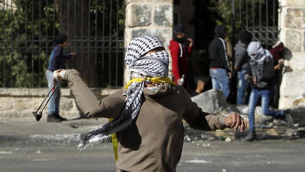 A Palestinian protestors throws a rock towards Israeli security forces during clashes at the main entrance of the occupied West Bank town of Bethlehem - Sputnik International