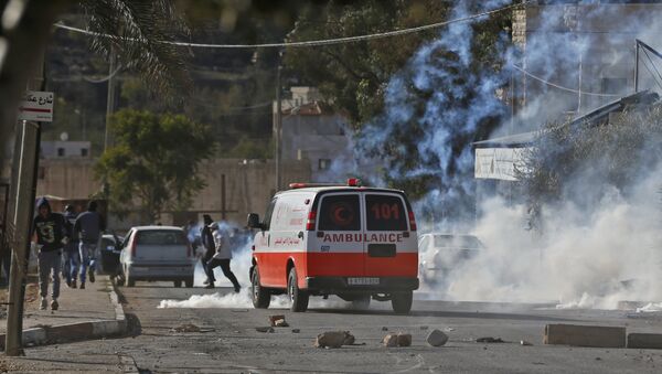 A Palestinian ambulance is seen driving amid teargas canisters shot by Israeli soldiers during clashed in the northern village of Qusra in the occupied West Bank near Nablus on December 4, 2017 - Sputnik International