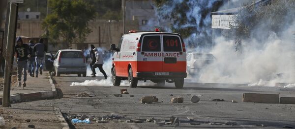 A Palestinian ambulance is seen driving amid teargas canisters shot by Israeli soldiers during clashed in the northern village of Qusra in the occupied West Bank near Nablus on December 4, 2017 - Sputnik International