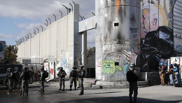 Israeli forces stand near the controversial separation barrier bearing graffiti depecting US President Donald Trump during clashes with Palestinian protestors near an Israeli checkpoint in the West Bank city of Bethlehem on December 7, 2017 - Sputnik International
