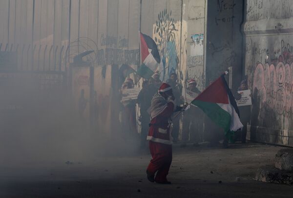 A Palestinian dressed as Santa Claus reacts from tear gas fired by Israeli troops during clashes in the West Bank city of Bethlehem, December 23, 2017 - Sputnik International