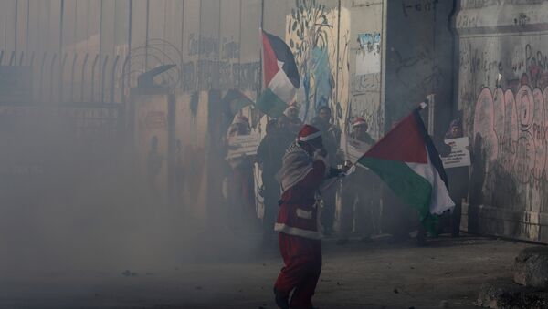 A Palestinian dressed as Santa Claus reacts from tear gas fired by Israeli troops during clashes in the West Bank city of Bethlehem, December 23, 2017 - Sputnik International