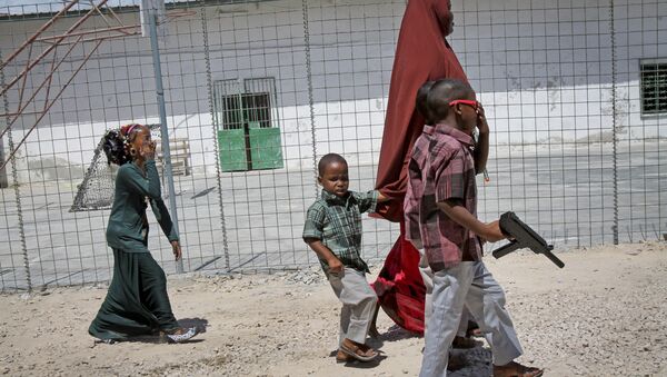 In this photo from 4 October 2014, a Somali mother walks with her children, one carrying a plastic toy gun, towards an area with children's toys to play with at the Mogadishu Guest House in Mogadishu, Somalia - Sputnik International