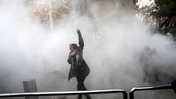 FILE - In this Saturday, Dec. 30, 2017 file photo taken by an individual not employed by the Associated Press and obtained by the AP outside Iran, a university student attends a protest inside Tehran University while a smoke grenade is thrown by anti-riot Iranian police, in Tehran, Iran - Sputnik International