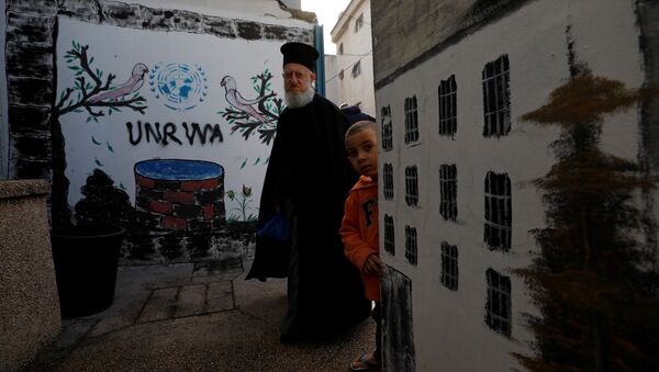 A Palestinian man walks past a logo of United Nations Relief and Works Agency (UNRWA) in Jalazone refugee camp, near the West Bank city of Ramallah January 3, 2018 - Sputnik International