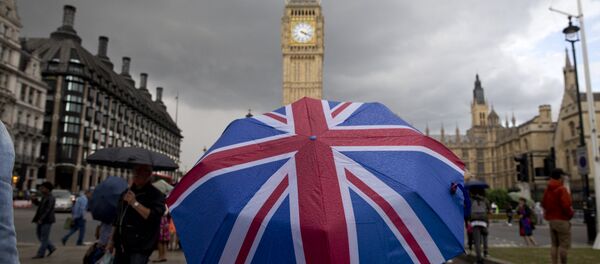 A pedestrian shelters from the rain beneath a Union flag themed umbrella as they walk near the Big Ben clock face and the Elizabeth Tower at the Houses of Parliament in central London. (File) - Sputnik International