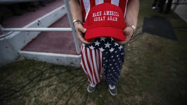A man dressed in American flag clothes holds Make America Great Again hats before President-elect Donald Trump speaks at a rally at the Ladd–Peebles Stadium, Saturday, Dec. 17, 2016, in Mobile, Ala. - Sputnik International