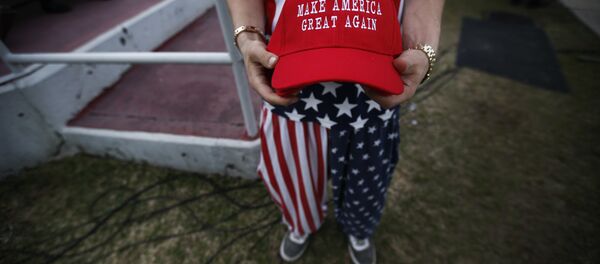 A man dressed in American flag clothes holds Make America Great Again hats before President-elect Donald Trump speaks at a rally at the Ladd–Peebles Stadium, Saturday, Dec. 17, 2016, in Mobile, Ala. - Sputnik International