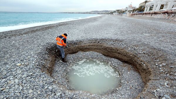 People looks at a two-metre deep and five-meter wide crater, filled with brackish water, which has formed on the beach of Lido on the French riviera city of Nice on February 1, 2018 - Sputnik International