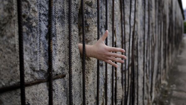 A tourist from the Netherlands puts his hand through a hole of the remains of the Berlin Wall to over a hand shake, at the Berlin Wall memorial at Bernauer Strasse in Berlin, Sunday, Aug. 13, 2017 - Sputnik International