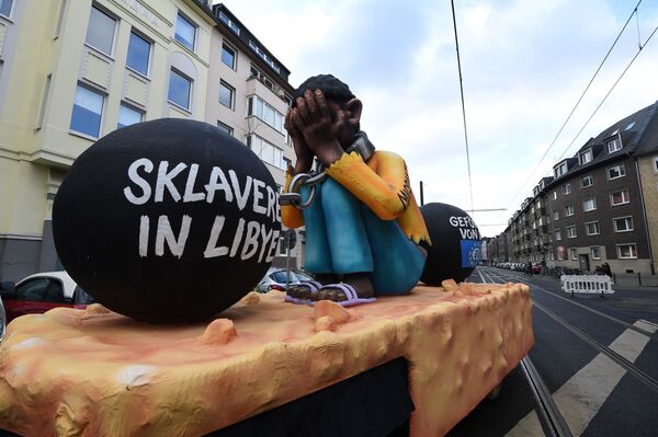 A carnival float, depicting a migrant with chains with the writings Slavery in Libya and supported by the EU, is pictured during a carnival parade on Rose Monday on February 12, 2018 in Duesseldorf, western Germany - Sputnik International