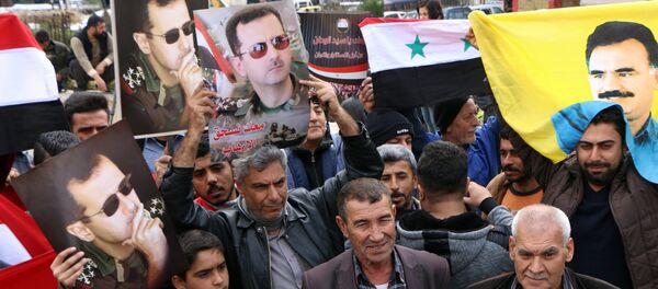 A picture taken on February 22, 2018 shows people waving the Syrian flag and portraits of President Bashar al-Assad and Kurdistan Worker's Party (PKK) leader Abdullah Ocalan as a convoy of pro-Syrian government fighters arrives in Syria's northern region of Afrin A picture taken on February 22, 2018 shows people waving the Syrian flag and portraits of President Bashar al-Assad and Kurdistan Worker's Party (PKK) leader Abdullah Ocalan as a convoy of pro-Syrian government fighters arrives in Syria's northern region of Afrin - Sputnik International