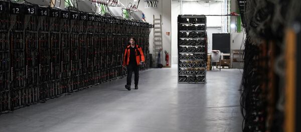 In this photo taken on Jan. 17, 2018, a worker walks along a row of computer rigs that run around the clock 'mining' bitcoin inside the Genesis Mining cryptocurrency mine in Keflavik, Iceland - Sputnik International