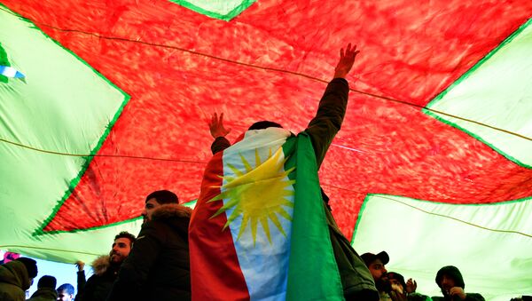 A demonstrator dressed in a Kurdistan flag cheers under a giant flag during a demonstration of Kurdish groups to protest against Turkey's offensive against Kurds in Syria's Afrin region, on March 3, 2018 in Berlin - Sputnik International