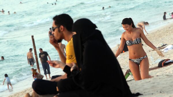 A foreign woman sunbathes near an Emirati couple on a beach in Dubai (File) - Sputnik International