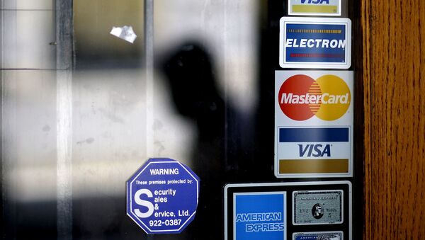 In this July 18, 2012, file photo, a pedestrian walks past credit card logos posted on a downtown storefront in Atlanta. After a stint of frugality, Americans have returned to their borrowing ways. But are they getting into the kinds of debt trouble that lead to recessions? In 2017, U.S. consumers now owe roughly $12.73 trillion to banks and other lenders for mortgages, car loans and credit card spending, according to the New York Federal Reserve. That exceeds even the total before the last financial crisis. - Sputnik International