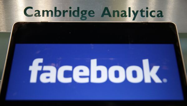 A laptop showing the Facebook logo is held alongside a Cambridge Analytica sign at the entrance to the building housing the offices of Cambridge Analytica, in central London - Sputnik International