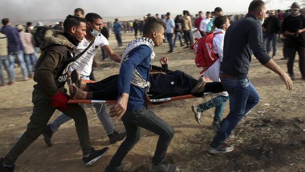 Palestinian protesters evacuate a wounded woman during clashes with Israeli troops along Gaza's border with Israel, Friday, April 13, 2018. - Sputnik International
