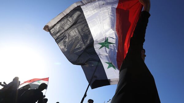 A Syrian government supporter holds up a Syrian national flag as he chants slogans against U.S. President Trump during demonstrations following a wave of U.S., British and French military strikes to punish President Bashar Assad for suspected chemical attack against civilians, in Damascus, Syria, Saturday, April 14, 2018 - Sputnik International