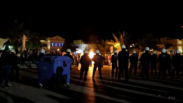 A garbage bin burns as riot police officers stand guard separating protesting groups of locals and refugees demonstrating against conditions in Moria camp and delays in asylum applications, in the city of Mytilene on the island of Lesbos, Greece, April 22, 2018 - Sputnik International