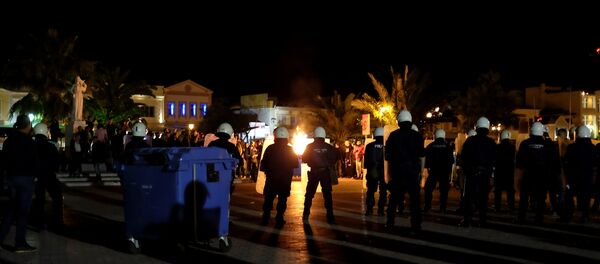 A garbage bin burns as riot police officers stand guard separating protesting groups of locals and refugees demonstrating against conditions in Moria camp and delays in asylum applications, in the city of Mytilene on the island of Lesbos, Greece, April 22, 2018 - Sputnik International