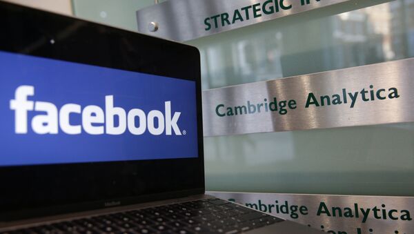 A laptop showing the Facebook logo is held alongside a Cambridge Analytica sign at the entrance to the building housing the offices of Cambridge Analytica, in central London on March 21, 2018 - Sputnik International