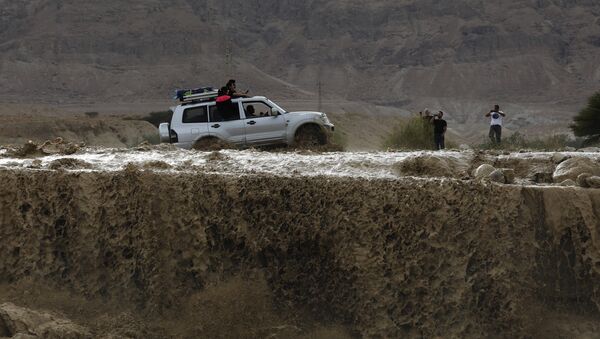 A car drives through flooded water running through a valley blocking the main road along the Dead Sea in the Judean desert, near the desert fortress of Masada north of Ein Bokek, following heavy rainfall in the mountains on April 25, 2018 - Sputnik International