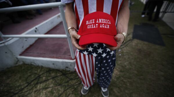 A man dressed in American flag clothes holds Make America Great Again hats. - Sputnik International
