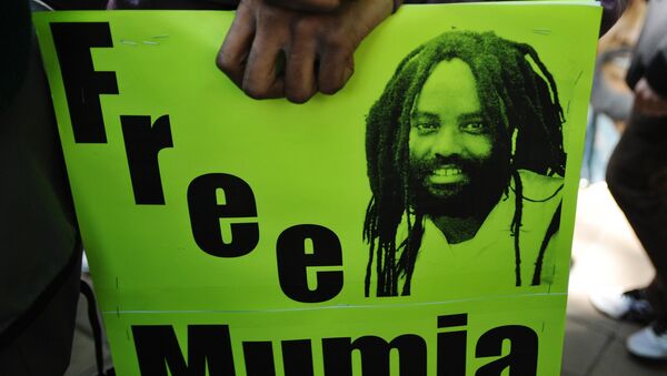 Protestors stand before an image of Mumia Abu-Jamal outside the US Department of Justice on April 24, 2012 in Washington, DC, calling for the release from prison of the ex-Black Panther militant, who was convicted for the killing of a white police officer in 1981 and sentenced to death. - Sputnik International