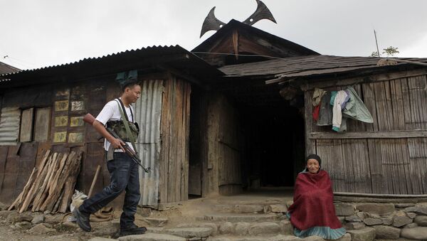 An armed cadre of the National Socialist Council of Nagaland (NSCN-IM), left, walks past an elderly woman sitting outside a traditional Naga hut, during a visit by the NSCN-IM General-Secretary Thuingaleng Muivah, at Viswema village, about 25 kilometers (16 miles) south of Kohima, capital of the northeastern Indian state of Nagaland (File) - Sputnik International