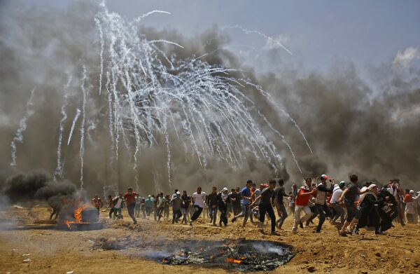 Palestinians run for cover from tear gas during clashes with Israeli security forces near the border between Israel and the Gaza Strip, east of Jabalia on May 14, 2018 Palestinians run for cover from tear gas during clashes with Israeli security forces near the border between Israel and the Gaza Strip, east of Jabalia on May 14, 2018 - Sputnik International