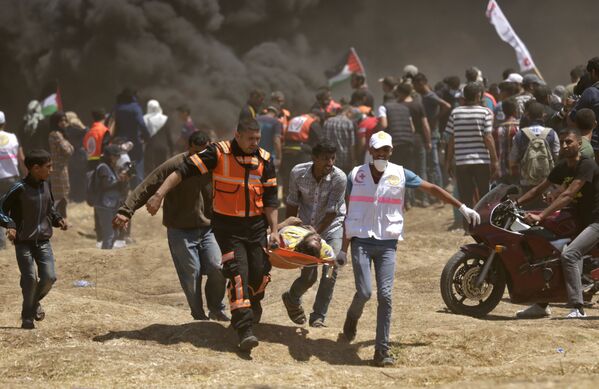 Palestinians carry a demonstrator injured during clashes with Israeli forces near the border between the Gaza strip and Israel east of Gaza City on May 14, 2018, as Palestinians readied for protests over the inauguration of the US embassy following its controversial move to Jerusalem - Sputnik International