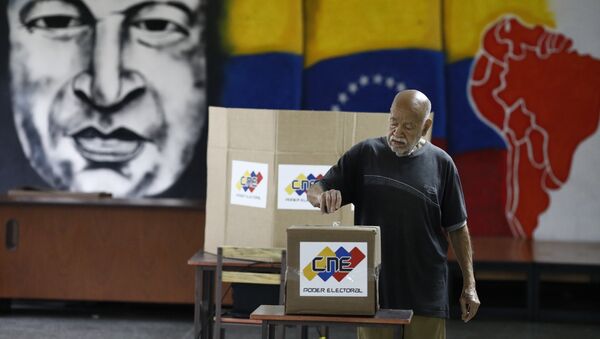 With an image of the late Venezuelan President Hugo Chavez behind him a Venezuelan citizen casts his vote at a polling station during the presidential election in Caracas, Venezuela, May 20, 2018 - Sputnik International