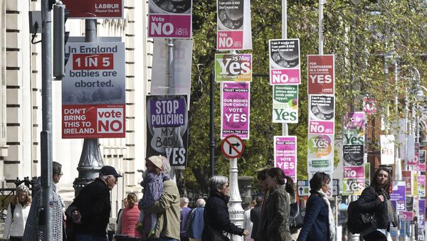 People cross the road past posters urging a yes vote in the referendum to repeal the eighth amendment of the Irish constitution, a subsection that effectively outlaws abortion in most cases, and posters calling for a no vote in the referendum near the government buildings in Dublin on May 12, 2018 - Sputnik International