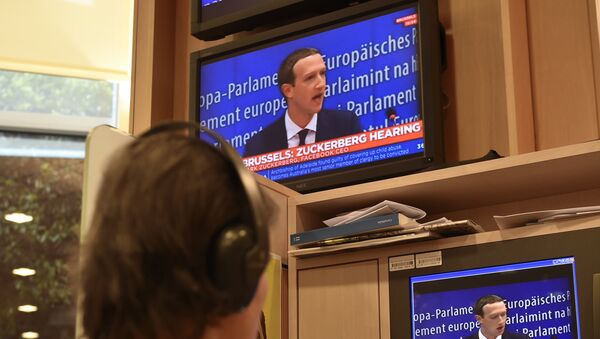 A journalist watches the speech of Facebook CEO Mark Zuckerberg on a television screen, in the press room, during his audition on the data privacy scandal on May 22, 2018 at the European Union headquarters in Brussels - Sputnik International