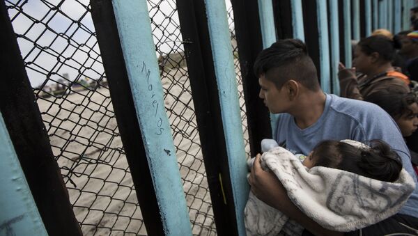In this April 29, 2018 file photo, a member of the Central American migrant caravan, holding a child, looks through the border wall toward a group of people gathered on the U.S. side, as he stands on the beach where the border wall ends in the ocean, in Tijuana, Mexico, Sunday, April 29, 2018 - Sputnik International