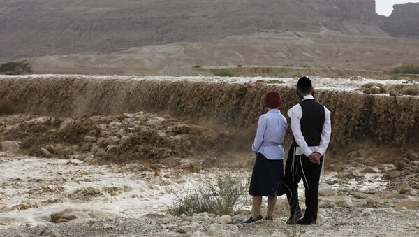 (File) Ultra-orthodox Jews watch flooded water running through a valley blocking the main road along the Dead Sea in the Judean desert, near the desert fortress of Masada north of Ein Bokek, following heavy rainfall in the mountains on April 25, 2018 - Sputnik International
