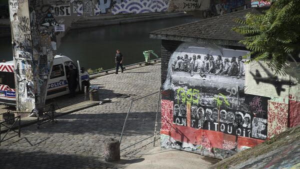 French police officer patrol past a mural depicting migrants (L) and an aeroplane (R) with the words underneath that read, 'What do we do?' painted and plastered on a structure along the banks of Canal Saint Martin where a former migrants camp was evacuated by the French authorities, on June 13, 2018 - Sputnik International