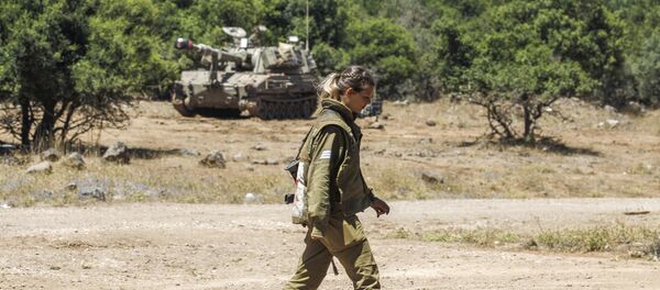 An Israeli soldier walks as a mobile artillery piece is seen deployed in the background near the border with Syria in the Israeli-annexed Syrian Golan Heights on July 1, 2018 - Sputnik International