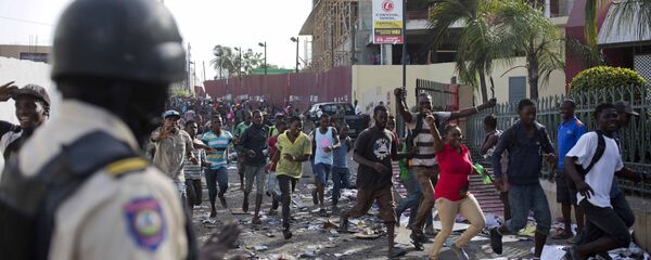 A police officer looks on as a crowd enters the Delimart supermarket complex, which had been burned during two days of protests against a planned hike in fuel prices in Port-au-Prince, Haiti, Sunday, July 8, 2018. A police officer looks on as a crowd enters the Delimart supermarket complex, which had been burned during two days of protests against a planned hike in fuel prices in Port-au-Prince, Haiti, Sunday, July 8, 2018. - Sputnik International