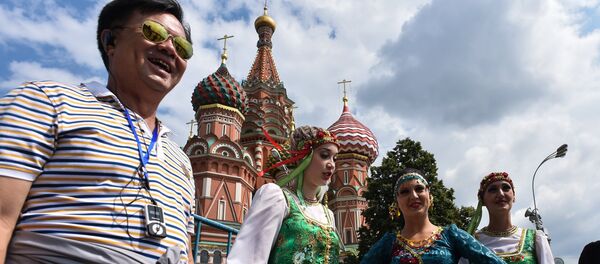 A tourist poses for a picture next to women wearing traditional dresses at Moscow's Red Square on July 10, 2015 A tourist poses for a picture next to women wearing traditional dresses at Moscow's Red Square on July 10, 2015 - Sputnik International