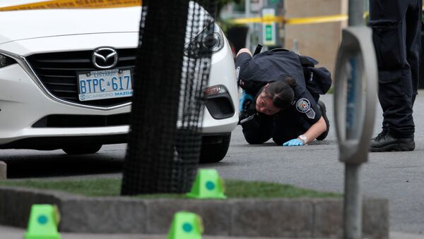 A police officer looks for evidence under a car while investigating a mass shooting on Danforth Avenue in Toronto, Canada, July 23, 2018. - Sputnik International